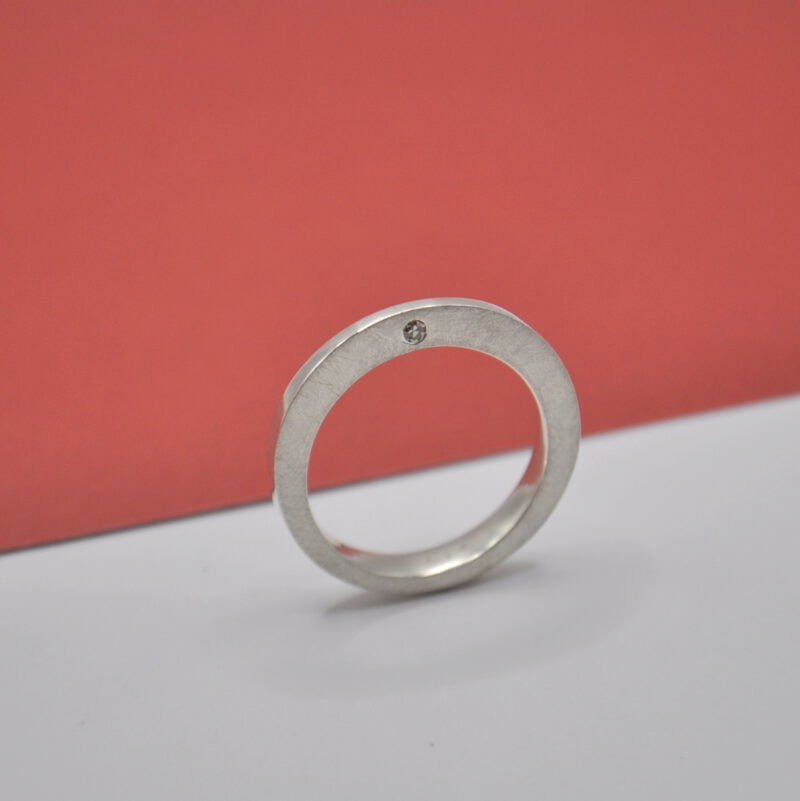 Ein Silberring ist von breit nach schmal verformt und hat einen eingefassten Diamant