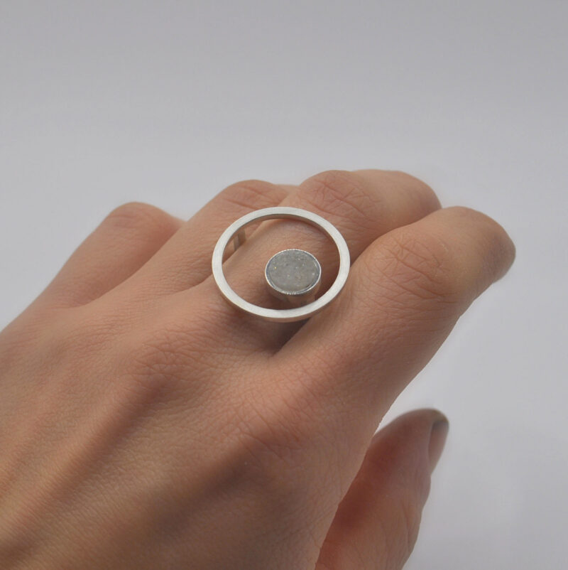 Ring mit Kreis aus Silber und weißem Kristall an einer Hand.