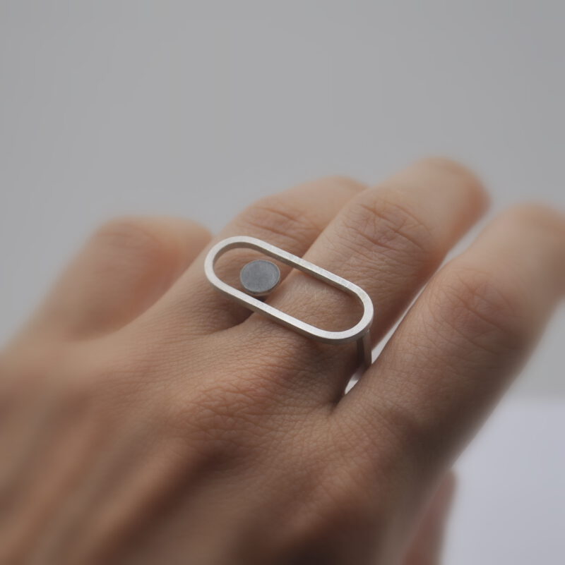 Ring "Geknöpft" an der Hand. Ein kleiner Kreis schwebt in einem Oval.