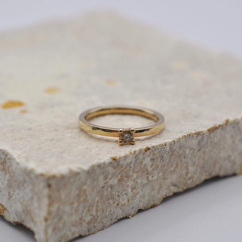 Antragsring aus Rosègold mit einem braunen Brillant liegt auf einer Platte