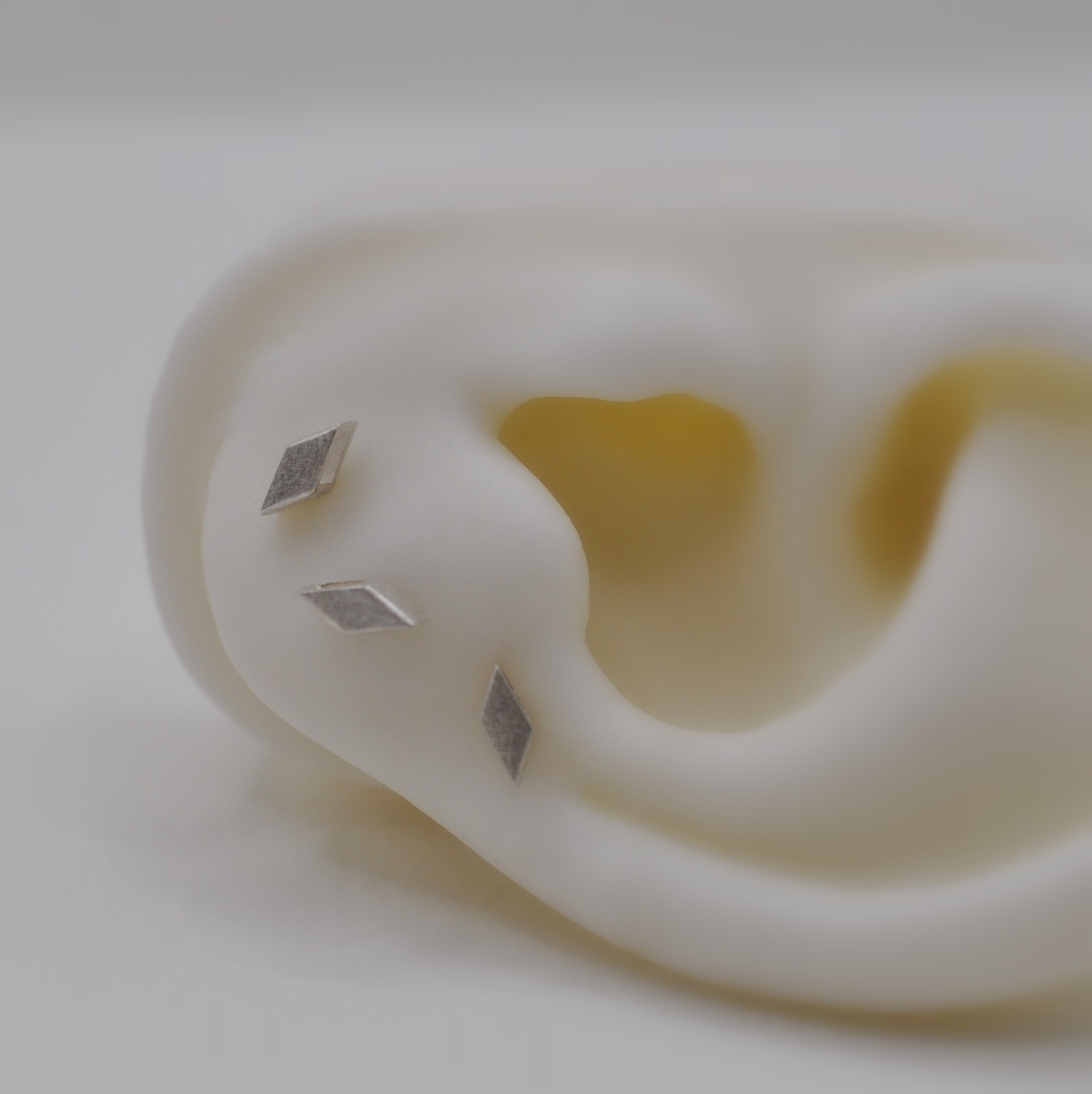 Drei silberne, rautenförmige Ohrstecker am Silikonohr