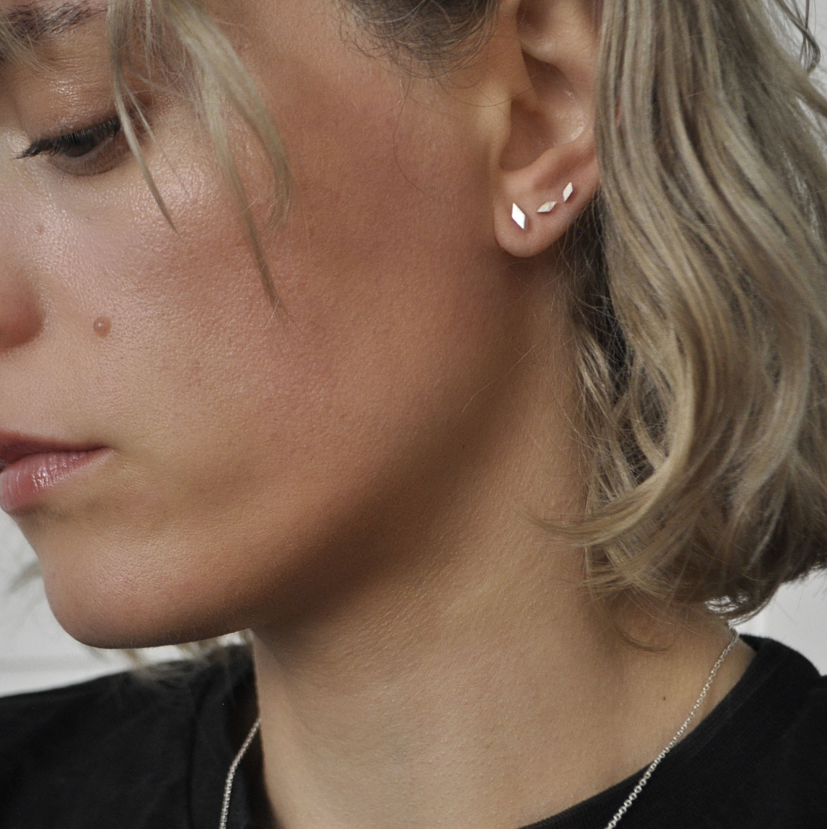 Frau mit drei kleinen Ohrsteckern in Form von schrägen Quadraten