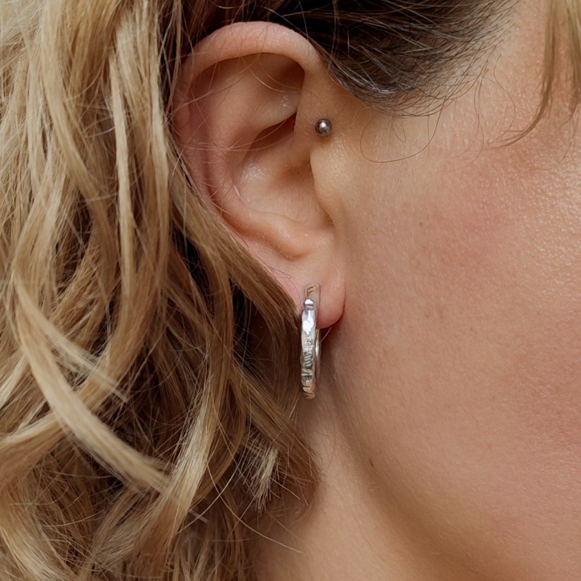 Nahaufnahme von silbernen Creolen mit unregelmäßiger Struktur am Ohr einer Frau