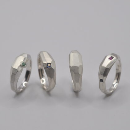 Vier Ringe, mit unregelmäßigen Facetten und teilweise eingefassten Steinen stehen nebeneinander