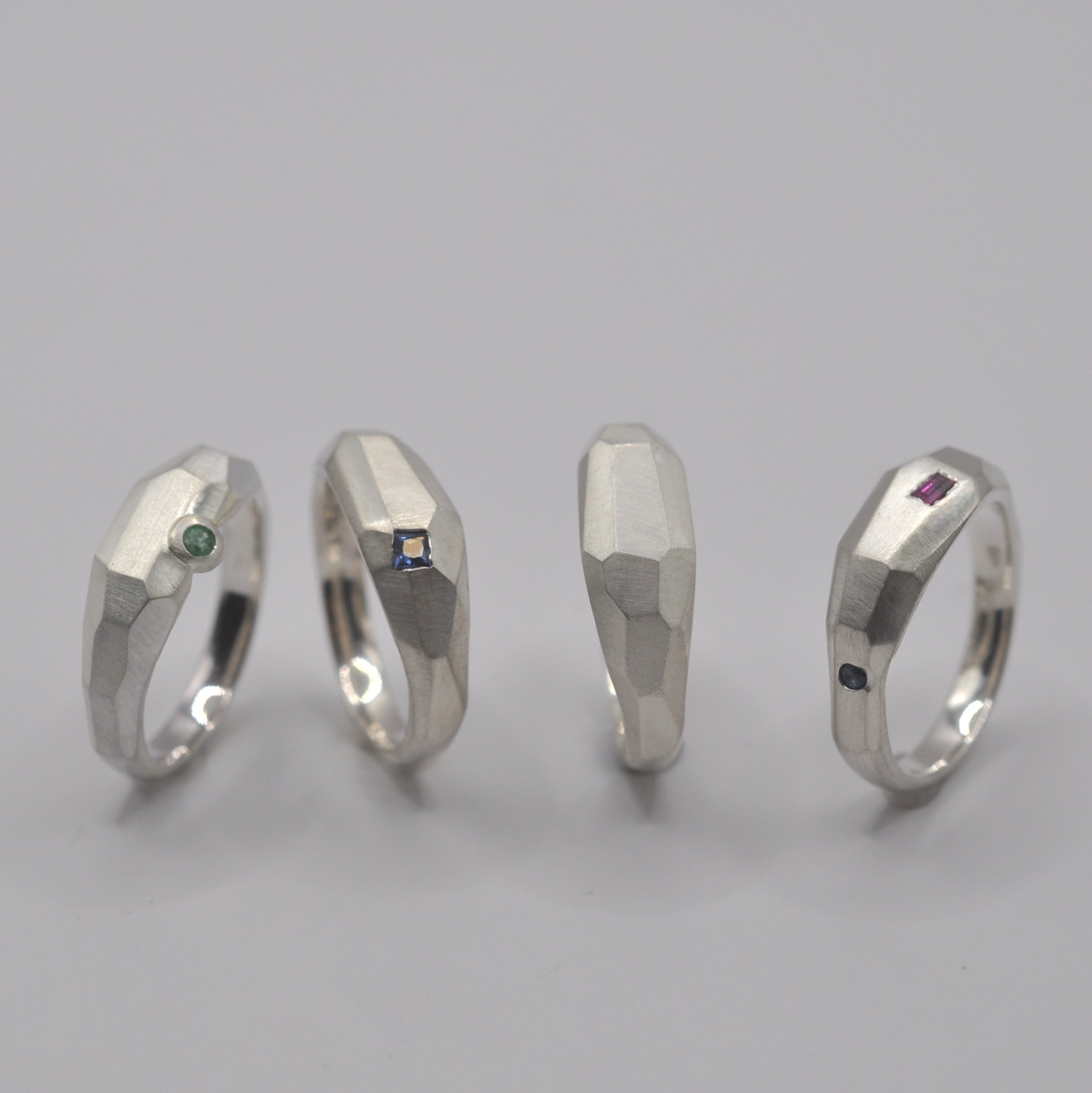 Vier Ringe, mit unregelmäßigen Facetten und teilweise eingefassten Steinen stehen nebeneinander