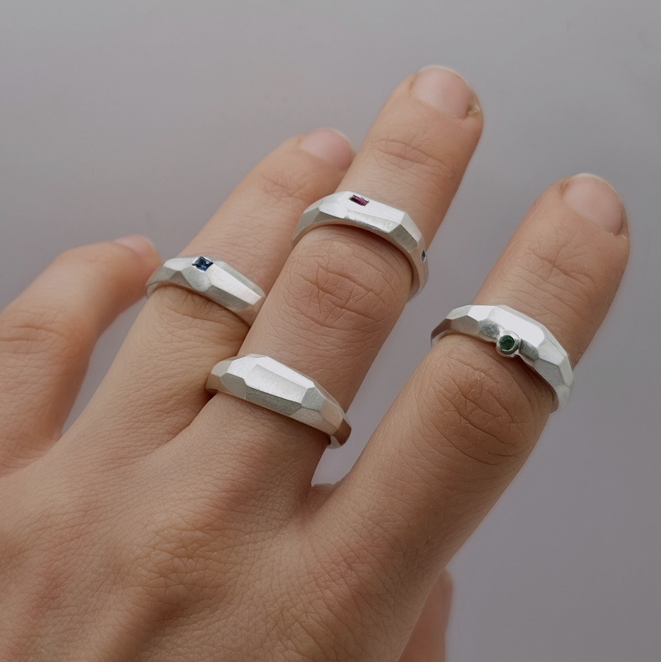 Vier Silberringe mit Flächen und Facetten an der Hand einer Frau. Teilweise sind Edlesteine eingefasst