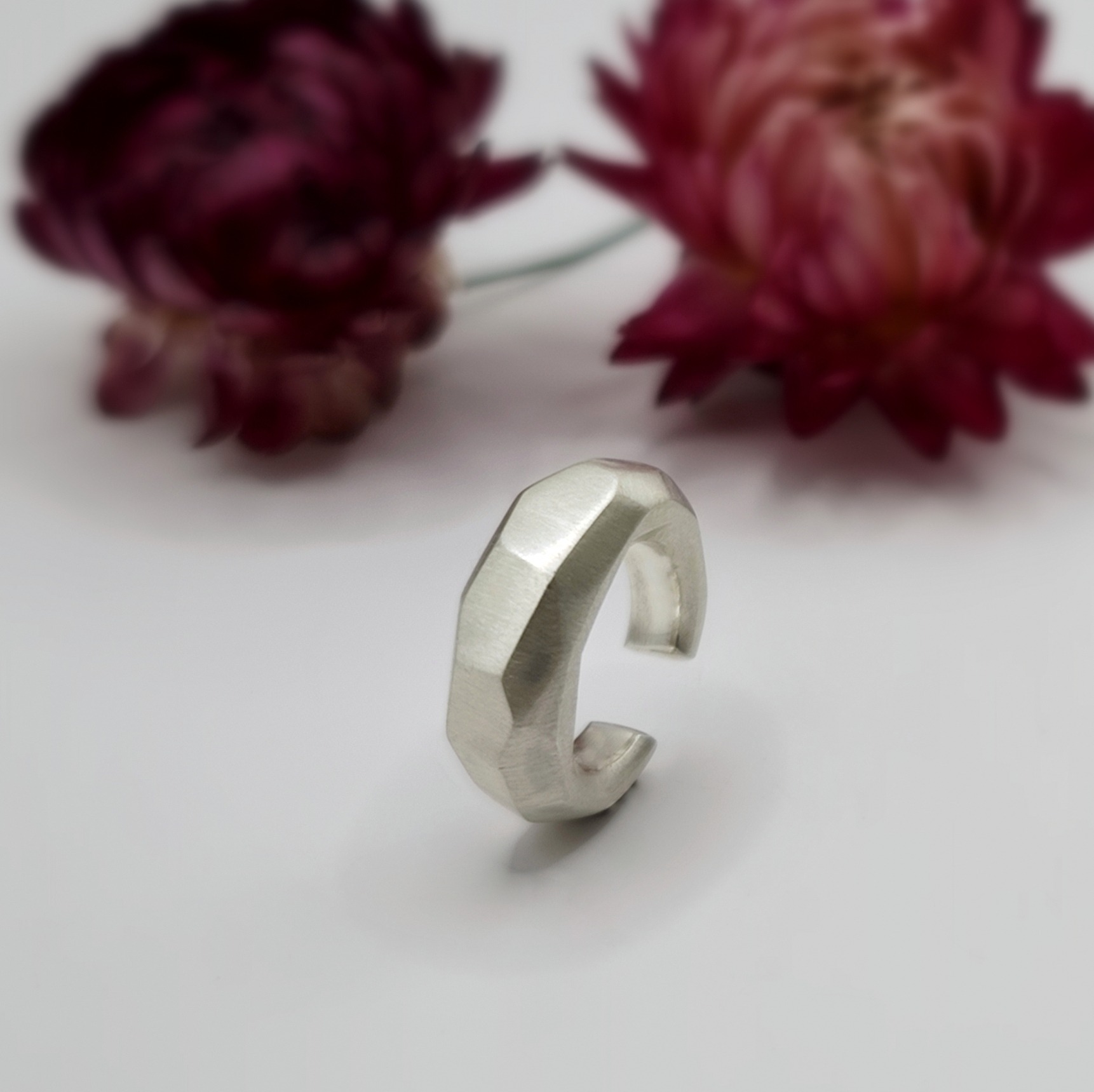 Seidenmatter Earcuff mit unregelmäßigen Facetten steht aufrecht vor Blumen